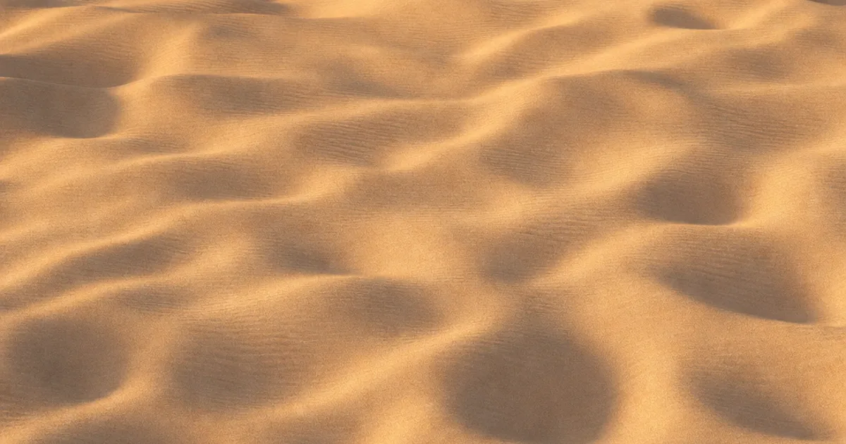 Photorealistic 3D render of golden desert sand with soft ripples tiled seamlessly across rolling dunes under warm low-angle light with no visible repeating pattern